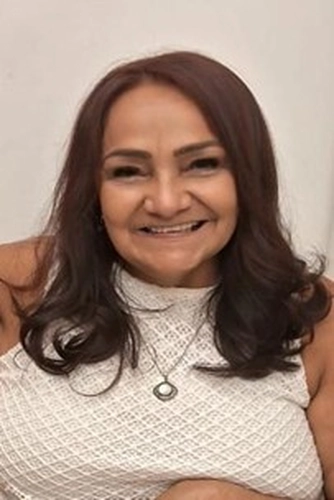 Mulher morena de cabelos médios lisos e blusa branca em um fundo branco.