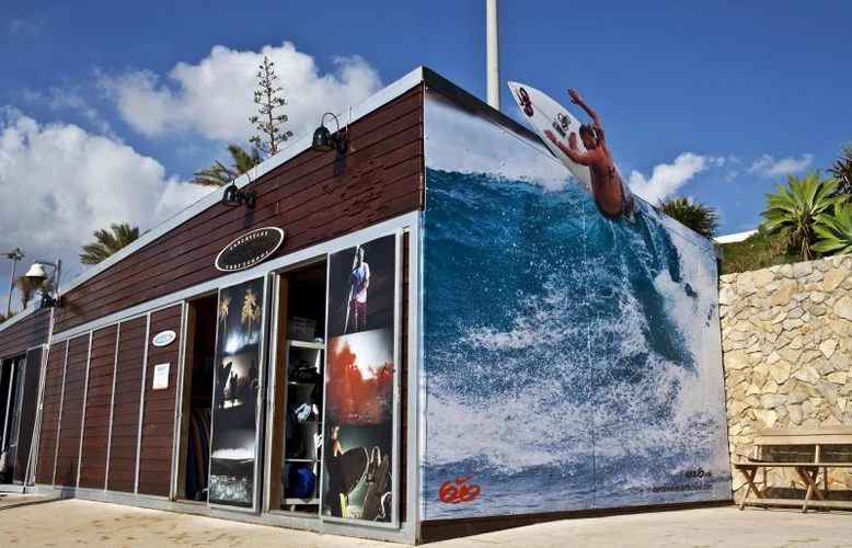 Loja de madeira e detalhes brancos com um quadro com a imagem do mar com ondas na laterar