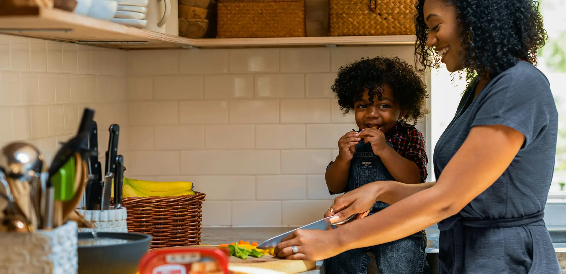 Mãe cortando legumes com o filho bebê ao lado.