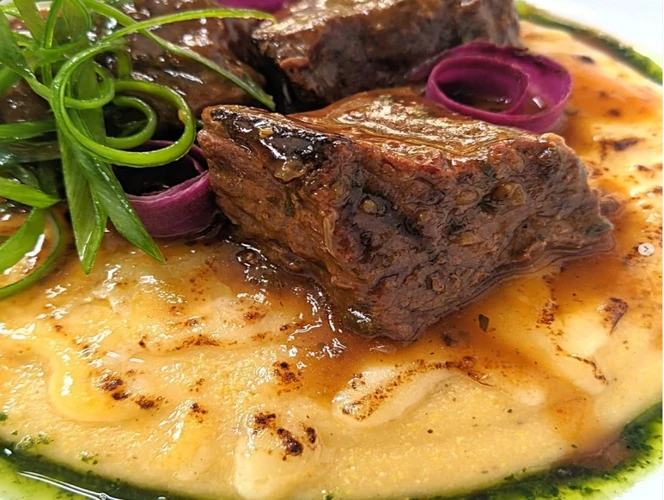 Prato de comida com uma base de creme de fubá, carne bovina refogada por cim com cebola roxa e erva verde de enfeite