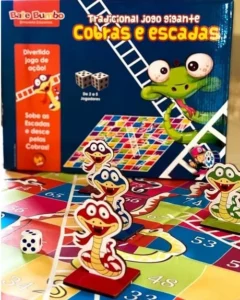 Jogo de tabuleiro infantil chamado "Cobras e Escadas" contém a imagem de uma cobra com a língua de fora e várias cobras de papel em cima de um tabuleiro com um dado.