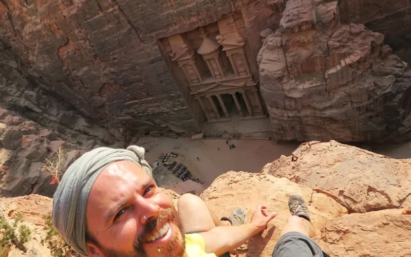 Pai na gestão de uma aventura, celebrando a liberdade e a conquista ao alcançar o topo de Ella's Rock, com uma vista deslumbrante das montanhas ao fundo.