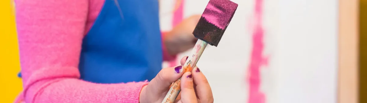 Criança segurando um pincel com a mão com tinta rosa.